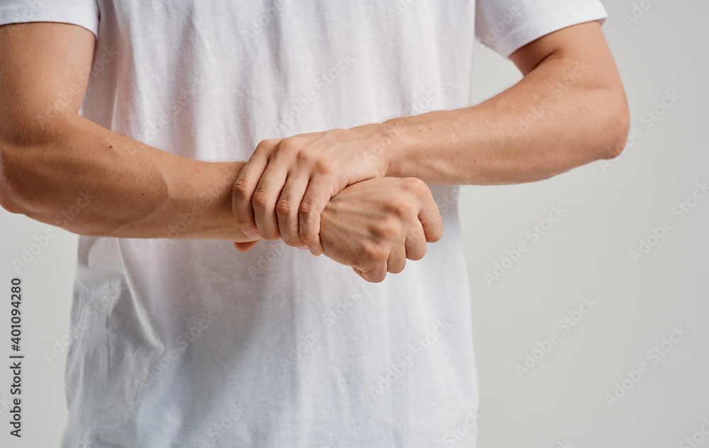 a man in a white t-shirt touches his wrists on a light background