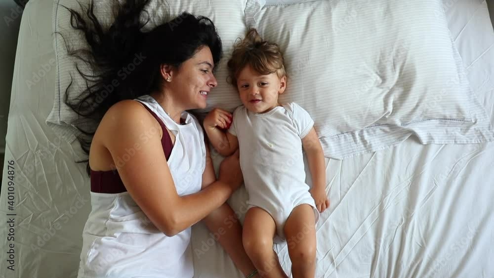 Mother and baby child son together in bed lying down, seen from above Mother and baby child son together in bed lying down, seen from above