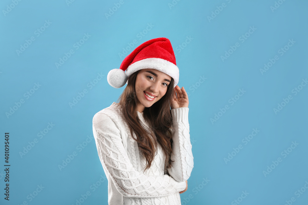 Beautiful woman wearing Santa Claus hat on light blue background Beautiful woman wearing Santa Claus hat on light blue background