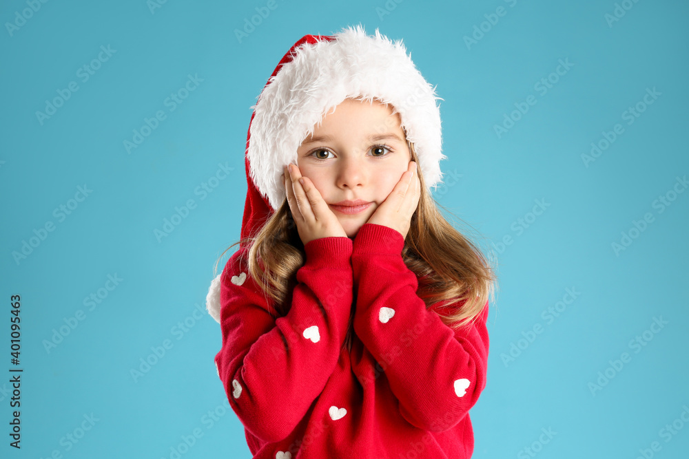 Cute child in Santa hat on light blue background. Christmas celebration Cute child in Santa hat on light blue background. Christmas celebration
