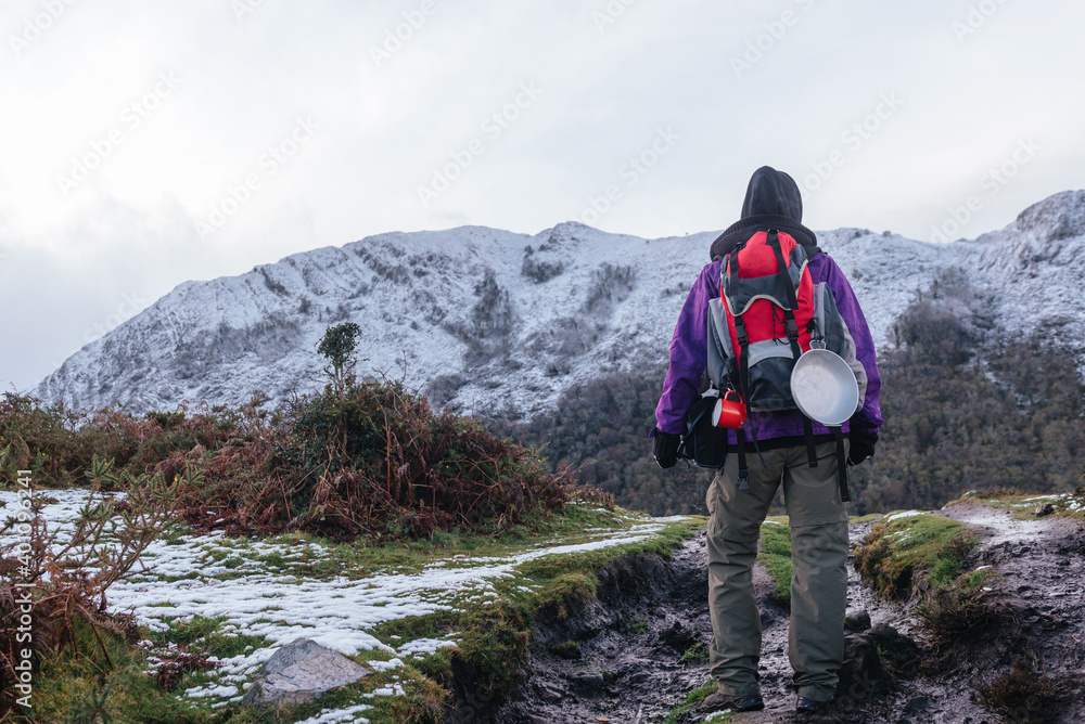 unrecognizable person hiking with a red backpack and camping utensils. He is ascending a snowy mountain in winter. winter sports.
