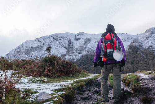 unrecognizable person hiking with a red backpack and camping utensils. He is ascending a snowy mountain in winter. winter sports. © Alberto