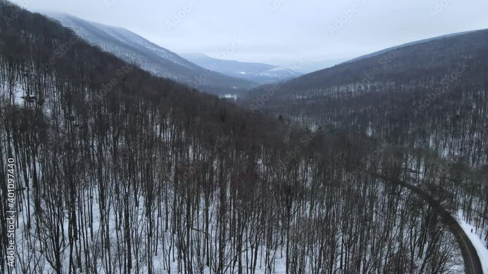 Flying over a snowy, beautiful mountain valley with a remote road below. Mountains in the background and forests as far as they eye can see Flying over a snowy, beautiful mountain valley with a remote road below. Mountains in the background and forests as far as they eye can see