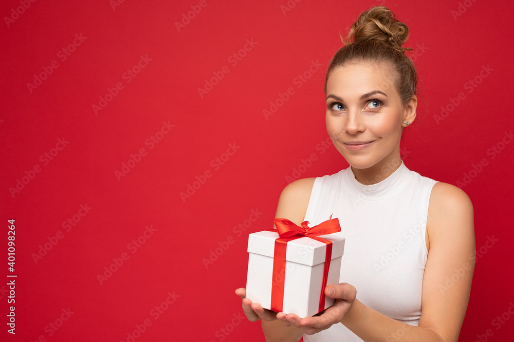 Beautiful happy young blonde woman isolated over colourful background wall wearing stylish casual clothes holding gift box and looking to the side Beautiful happy young blonde woman isolated over colourful background wall wearing stylish casual clothes holding gift box and looking to the side