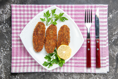 top view cutlets lemon slice parsley on white platefork and knife kitchen towel on grey background photo