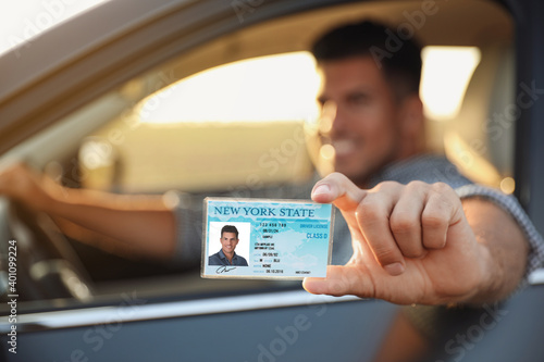Happy man holding license while sitting in car outdoors, focus on hand. Driving school photo