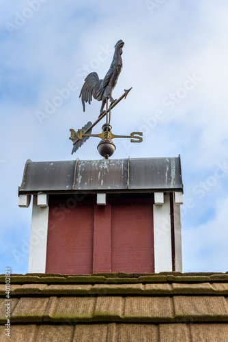 Copper rooster weathervane on top of red rooftop cupola with a blue sky and white clouds in the background
