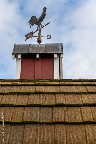 Canvas Print Copper rooster weathervane on top of red rooftop cupola with a blue sky and whit