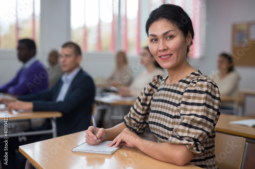 Young positive woman sitting at desk in classroom working during lesson at adult education class