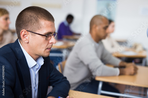 Portrait of focused male sitting at desk studying in classroom with colleagues