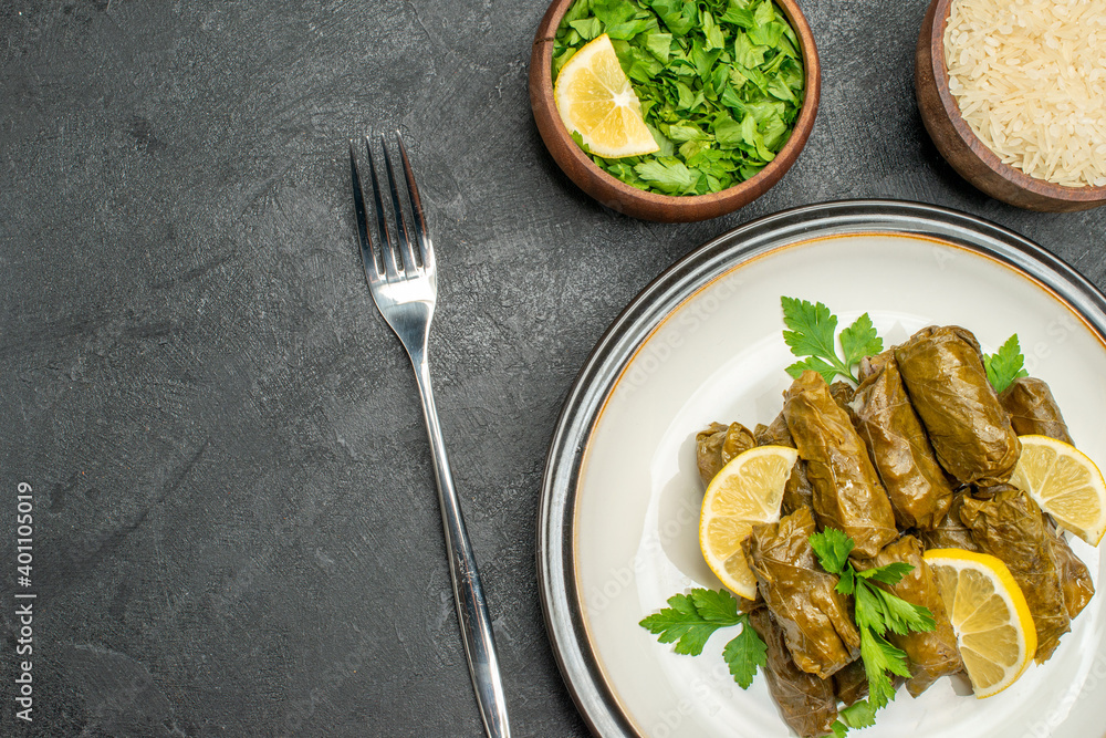top close view stuffed grape leaves on white plate bowls of parsley and rice a fork on dark background with free space top close view stuffed grape leaves on white plate bowls of parsley and rice a fork on dark background with free space