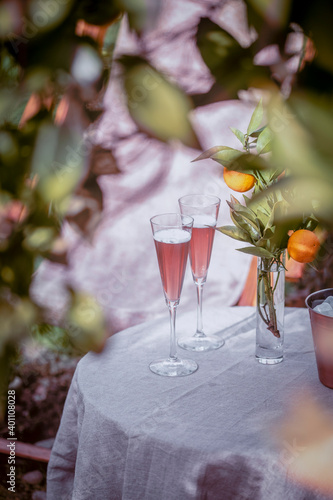 Table near the orange tree in the garden with two glasses of sparkling rose wine