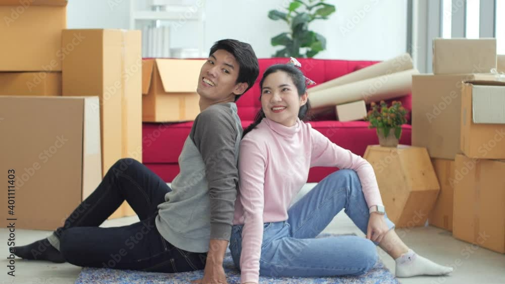 Portrait of young attractive happy asian couple man and woman sitting at new home with carton package box storage to move in empty house. Young married asian relocating home concept. Portrait of young attractive happy asian couple man and woman sitting at new home with carton package box storage to move in empty house. Young married asian relocating home concept.