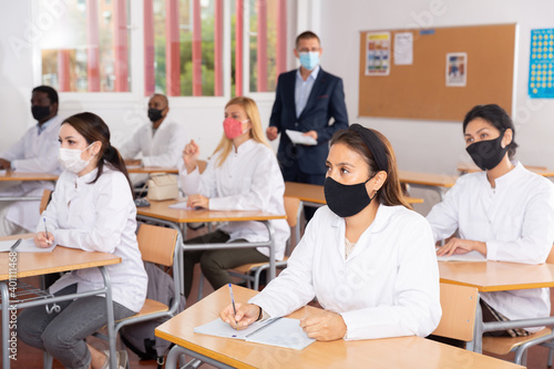 Focused adult medical students different nationalities wearing protective face masks to prevent viral infections attending refresher course. New life reality in coronavirus pandemic © JackF