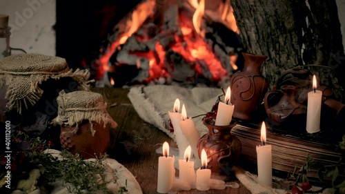 Preparation of items for witchcraft. Burning candles on the background of an open fire in the fireplace, dripping wax. Clay pots with components of poison. Concept of mysticism.