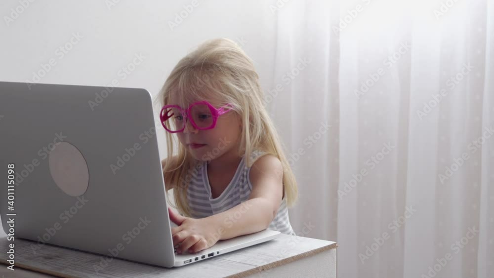 Little girl in funny glasses works at the computer at home