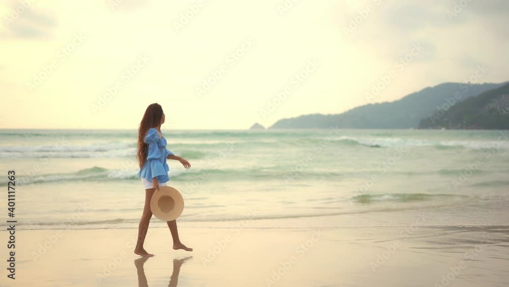 A pretty girl carrying her straw sun hats twirls around as she makes her way along a sandy beach at sunset. A pretty girl carrying her straw sun hats twirls around as she makes her way along a sandy beach at sunset.