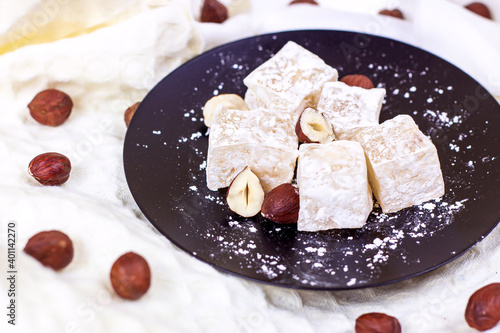 Traditional Turkish delight sweet homemade rahat lokum with hazelnuts and sugar powder on black plate.