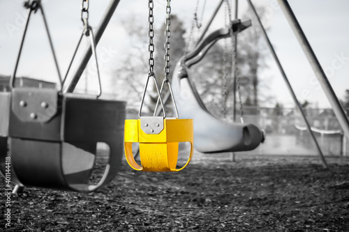 Playground swing set for toddlers with full bucket seats, close up. Black and white image with one seat in bright yellow accent color. Selective color. Concept for detect early signs of development.