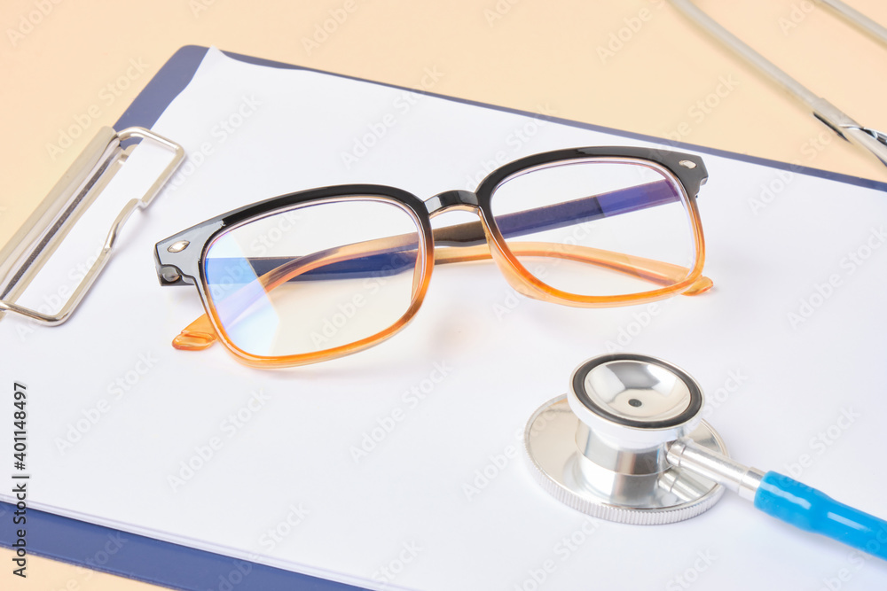 glasses and stethoscope on a clipboard beige background glasses and stethoscope on a clipboard beige background