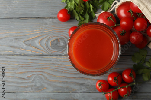 Glass of tomato juice and tomatoes on gray wooden table