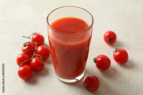 Glass of tomato juice and tomatoes on white textured background