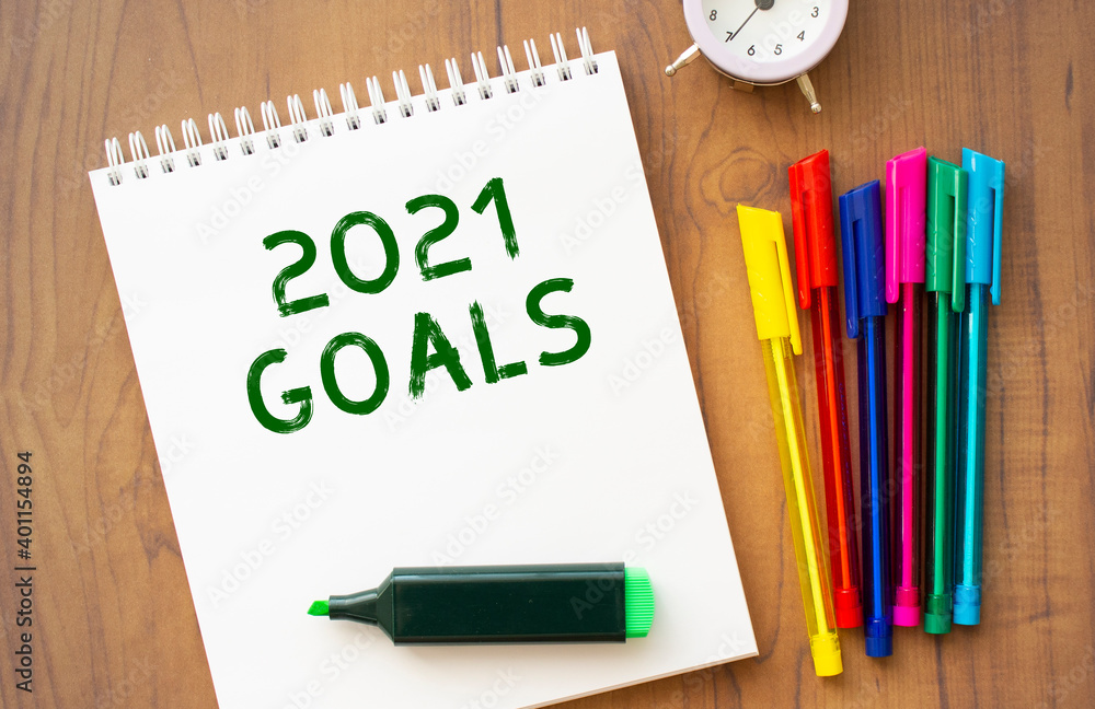 A notebook with the text 2021 GOALS lies on a brown wooden table. A notebook with the text 2021 GOALS lies on a brown wooden table.