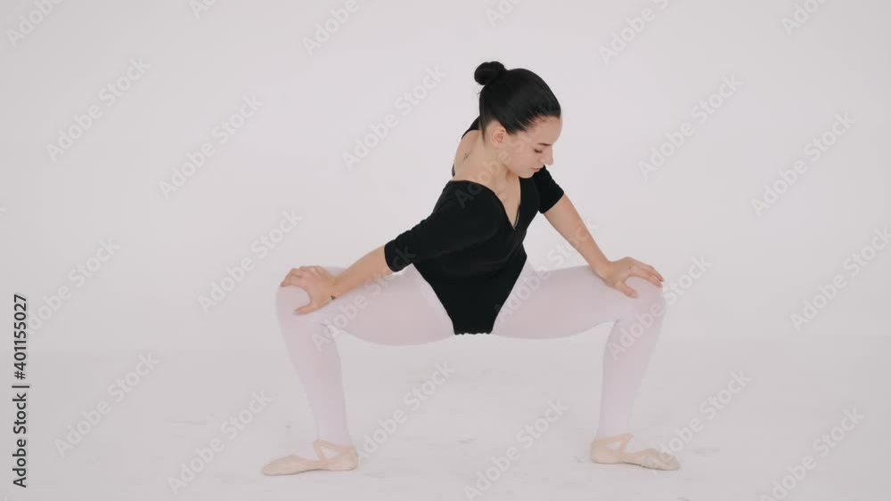 Dancer warms up her legs before rehearsal on the floor of white dance hall Dancer warms up her legs before rehearsal on the floor of white dance hall