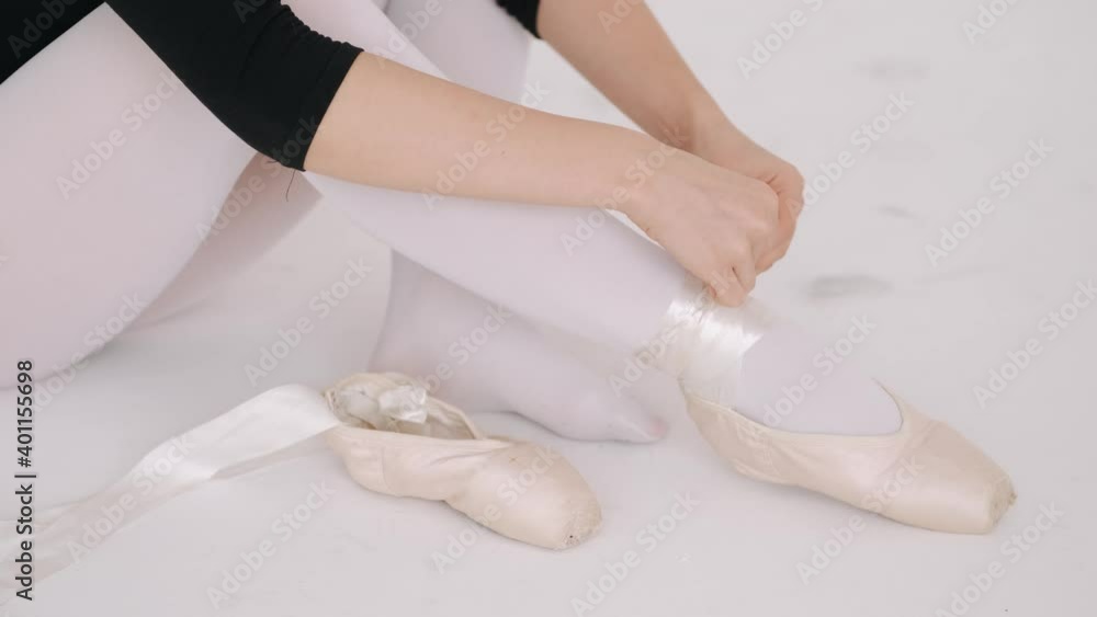 Young tired girl ballerina puts on her feet pointe shoes sitting in a studio. Young tired girl ballerina puts on her feet pointe shoes sitting in a studio.
