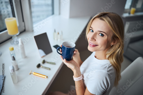 Charming elegant female looking at the photo camera while enjoying tasty beverage in room indoors