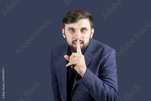 a male businessman in a blue suit puts a finger to his lips, indicating that everyone should be silent