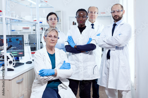Team of professional scientists standing together in research lab looking at camera posing with arms crossed. African healthcare scientist in biochemistry laboratory wearing sterile equipment.