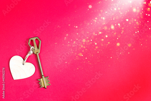 Golden key with wooden tag in the shape of a heart on a red background. Valentine's day, Declaration of love, copy space. Open, closed feelings. Sweet home, real estate