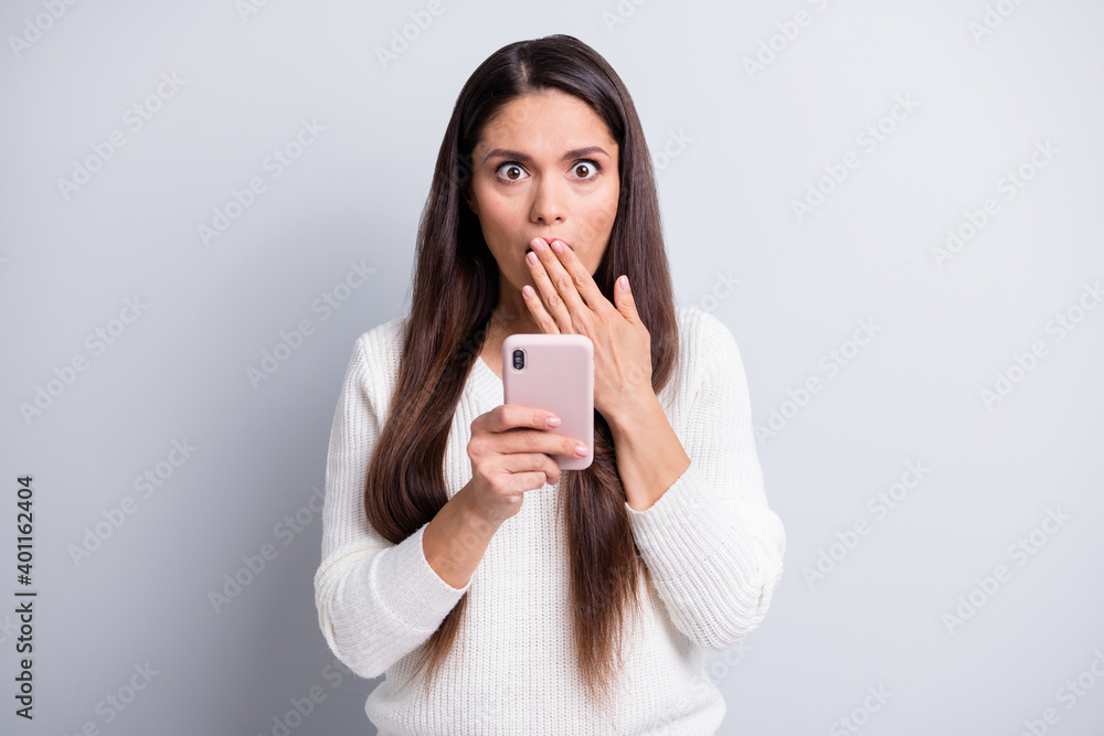 Photo of mature shocked surprised amazed beautiful woman cover mouth hold smartphone isolated on grey color background Photo of mature shocked surprised amazed beautiful woman cover mouth hold smartphone isolated on grey color background