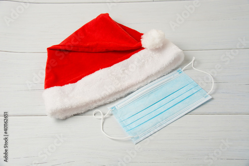 Santa claus hat and medical mask on a light wooden table close up copy space