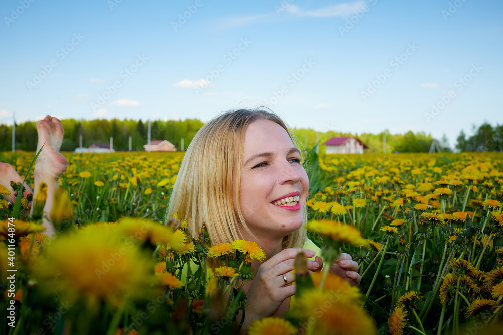 Pretty woman on a field with green grass and yellow dandelion flowers in a sunny day. Girl on nature with yellow flowers and blue sky. Pretty woman on a field with green grass and yellow dandelion flowers in a sunny day. Girl on nature with yellow flowers and blue sky.
