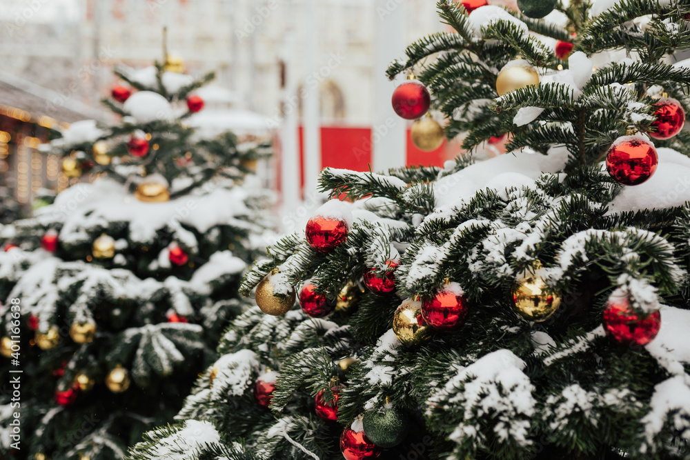 Snow on branches of Christmas trees decorated with red and golden balls on the city street. Christmas market.