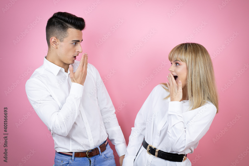 Young couple of girlfriend and boyfriend over isolated pink background with her hand over her mouth and surprised, looking side Young couple of girlfriend and boyfriend over isolated pink background with her hand over her mouth and surprised, looking side