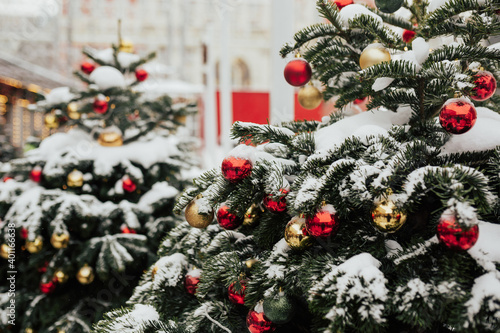 Obraz na płótnie Snow on branches of Christmas trees decorated with red and golden balls on the city street. Christmas market. w salonie