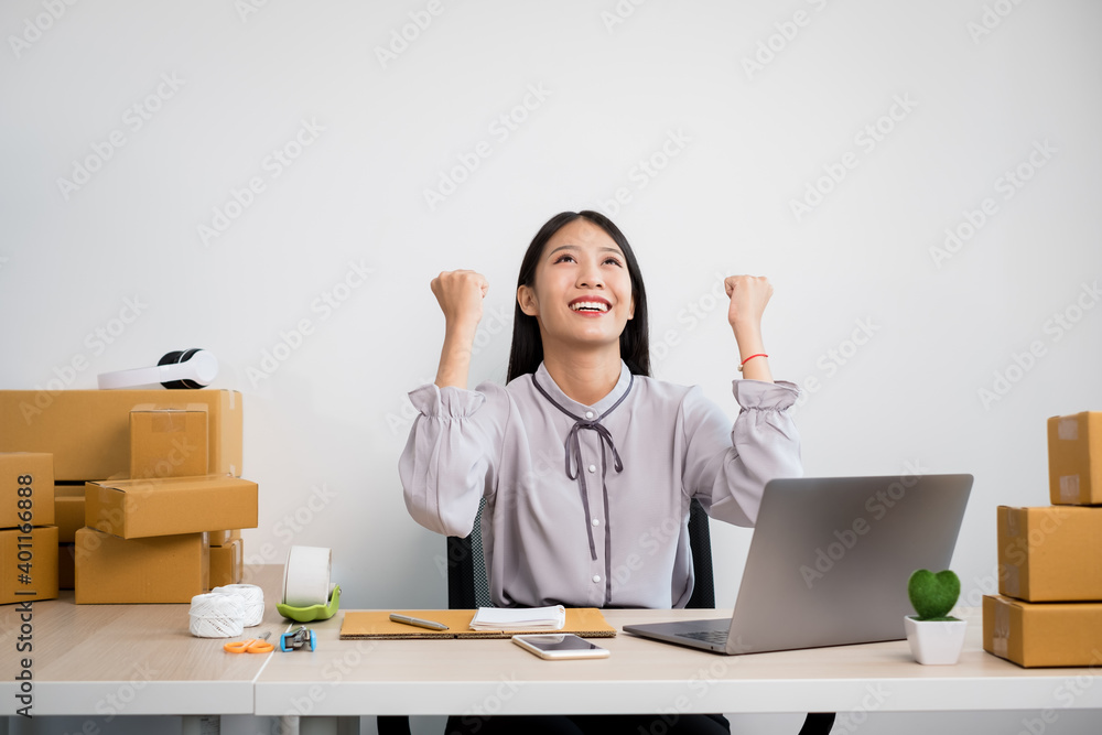 Young Asian woman business owner with many parcel boxes on the table happy online sales job, use your laptop, get an order from customers, take notes, and make arrangements for delivery by post Young Asian woman business owner with many parcel boxes on the table happy online sales job, use your laptop, get an order from customers, take notes, and make arrangements for delivery by post