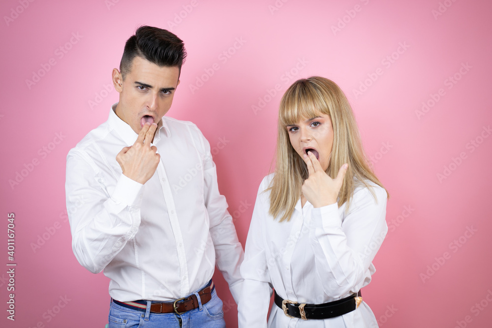 Young couple of girlfriend and boyfriend over isolated pink background disgusted with her hand inside her mouth Young couple of girlfriend and boyfriend over isolated pink background disgusted with her hand inside her mouth