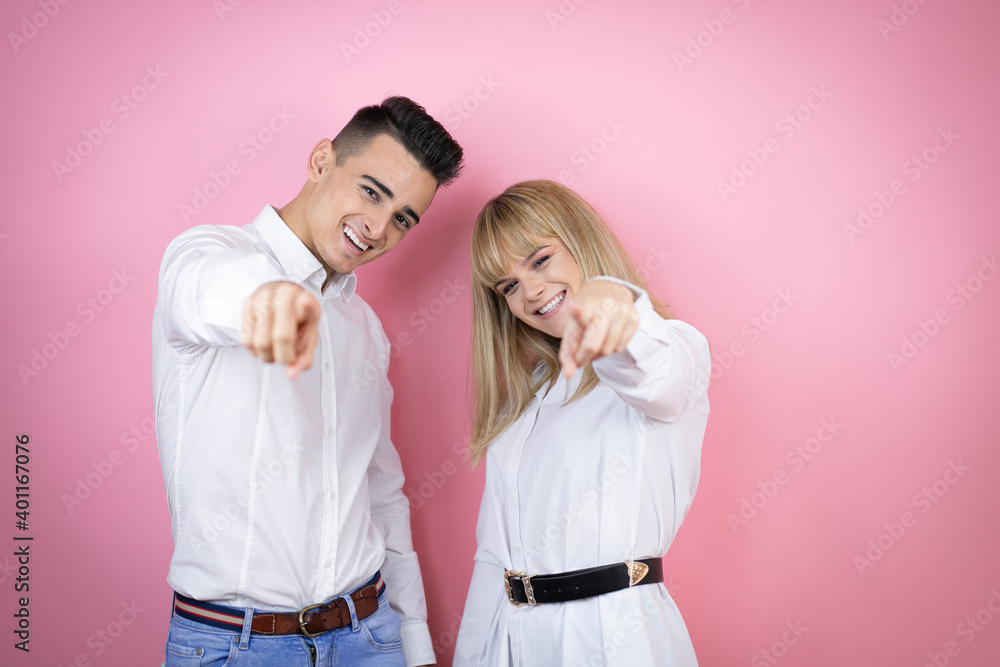 Young couple of girlfriend and boyfriend over isolated pink background laughing at you, pointing finger to the camera with hand over body, shame expression Young couple of girlfriend and boyfriend over isolated pink background laughing at you, pointing finger to the camera with hand over body, shame expression