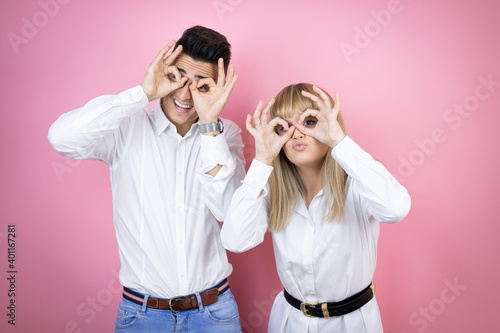 Young couple of girlfriend and boyfriend over isolated pink background doing ok gesture shocked with smiling face, eye looking through fingers