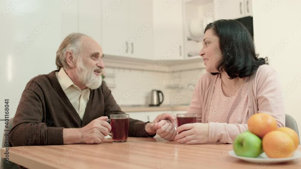 Happy old father talking to daughter, drinking tea together in kitchen, family