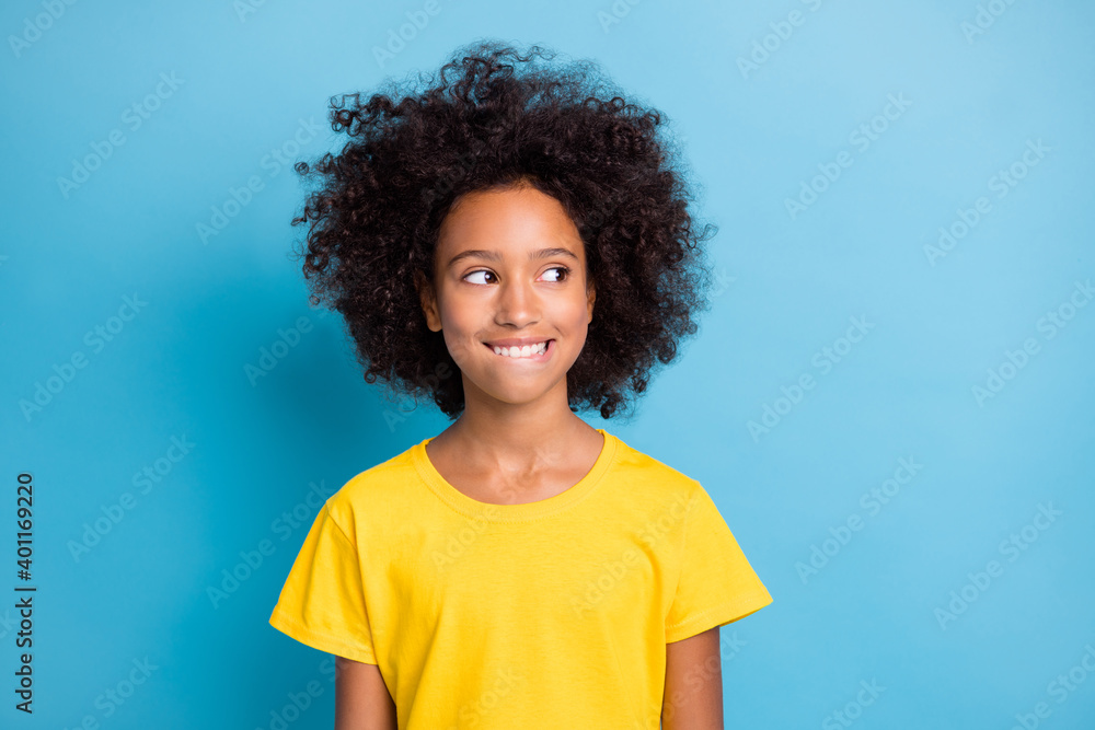 Photo of dreamy cute little afro american girl look empty space wear yellow t-shirt think bite lip isolated on blue color background Photo of dreamy cute little afro american girl look empty space wear yellow t-shirt think bite lip isolated on blue color background