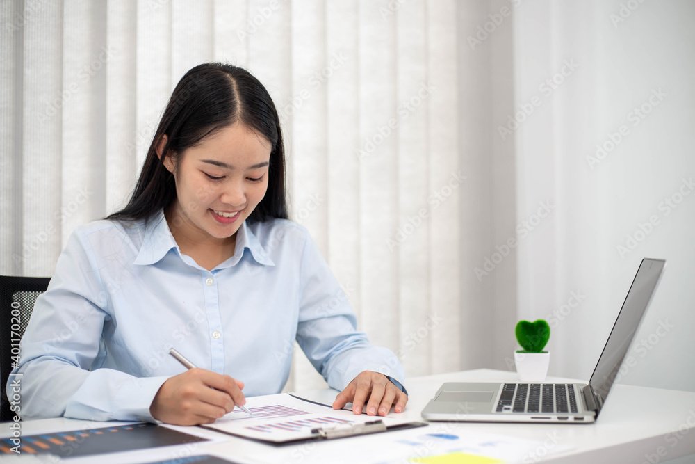 Portrait of businesswoman with laptop writes on a document and check graph at her office Portrait of businesswoman with laptop writes on a document and check graph at her office