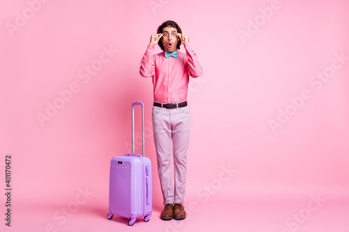 Full length photo of funny handsome surprised brunet hair man tourist arms spectacles luggage isolated pink color background