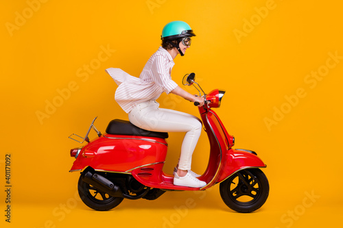 Side profile full length photo of pretty funky young girl riding motorbike enjoying highway trip wear white striped shirt pants helmet glasses isolated yellow vivid color background © deagreez