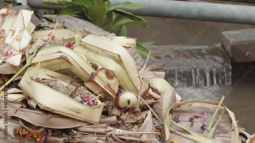 Canang Sari - Bali Offerings By Balinese Hindus In A Shrine In Indonesia With Flowing Water In Background - close up Canang Sari - Bali Offerings By Balinese Hindus In A Shrine In Indonesia With Flowing Water In Background - close up