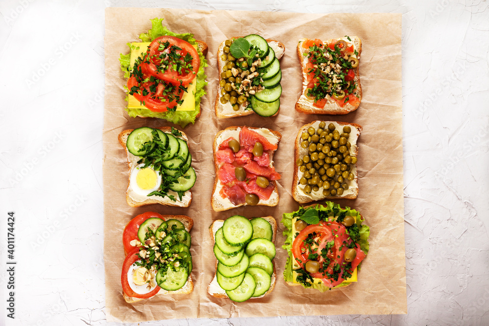 A variety of sandwiches with cream cheese, salmon, egg, herbs and vegetables on craft paper on a concrete background. Healthy food concept. A variety of sandwiches with cream cheese, salmon, egg, herbs and vegetables on craft paper on a concrete background. Healthy food concept.